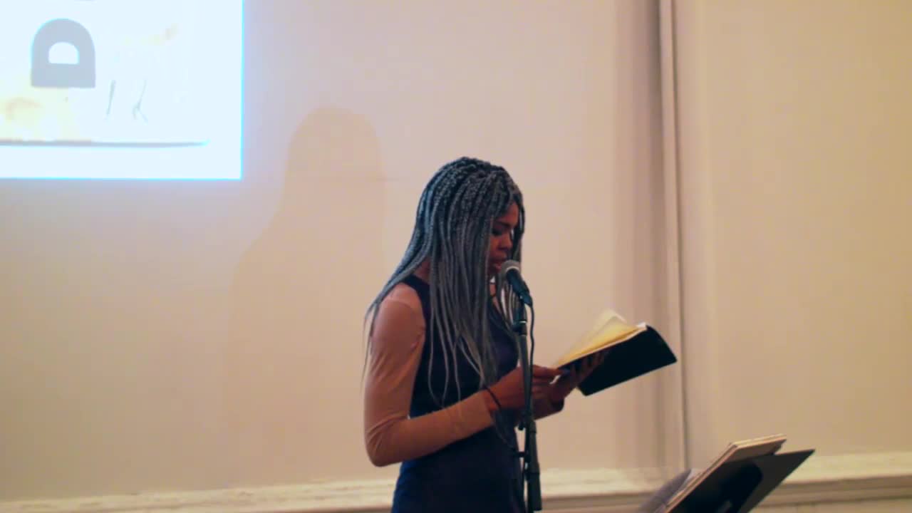 A person reads from several sheets of printed paper to an audience