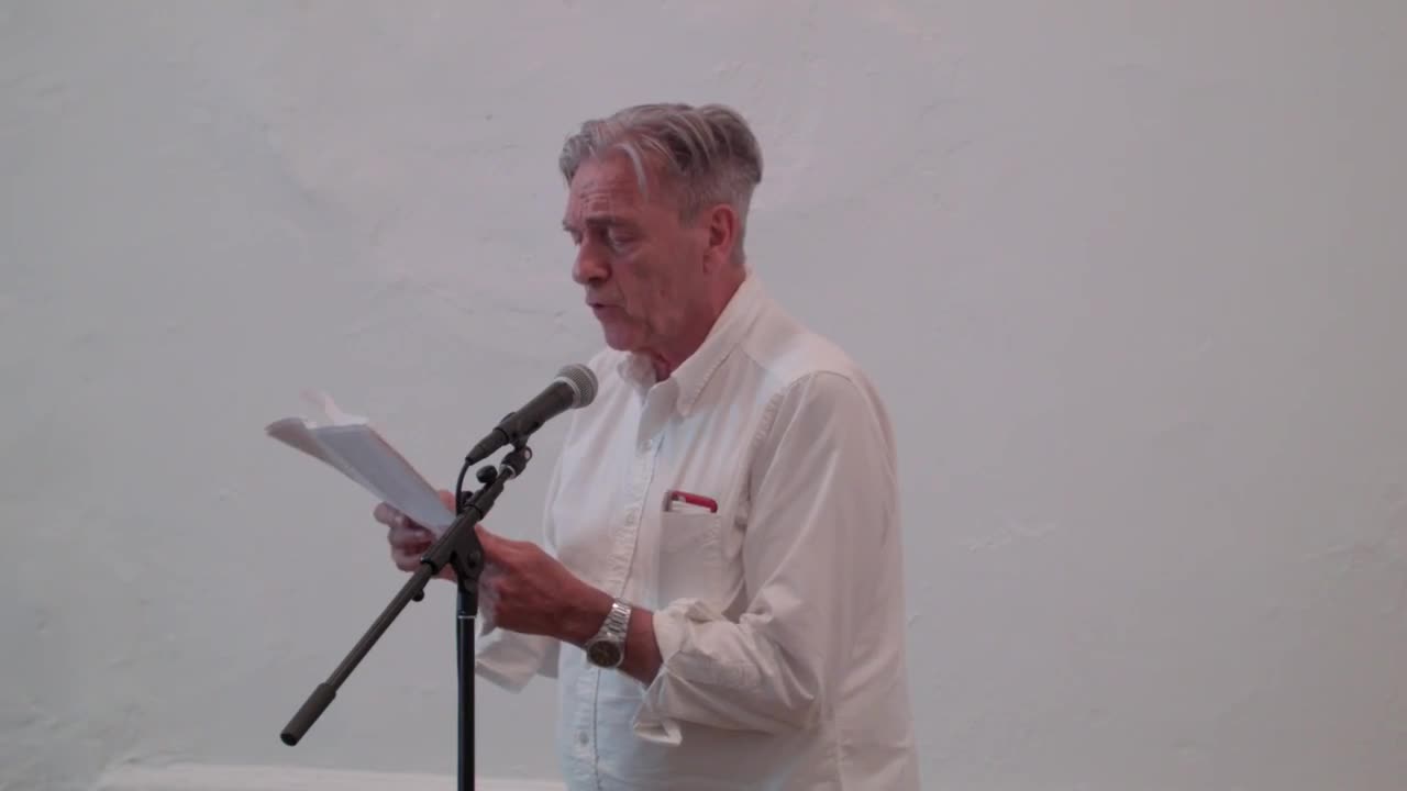 A person reading from a printed text in front of a small audience.