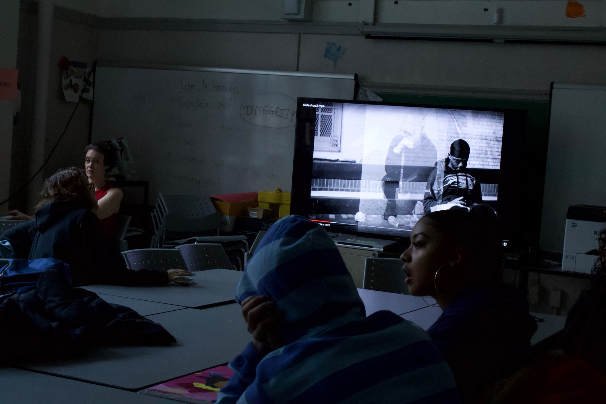 A photo of students sitting around a table, watching a YouTube video and speaking to one another.