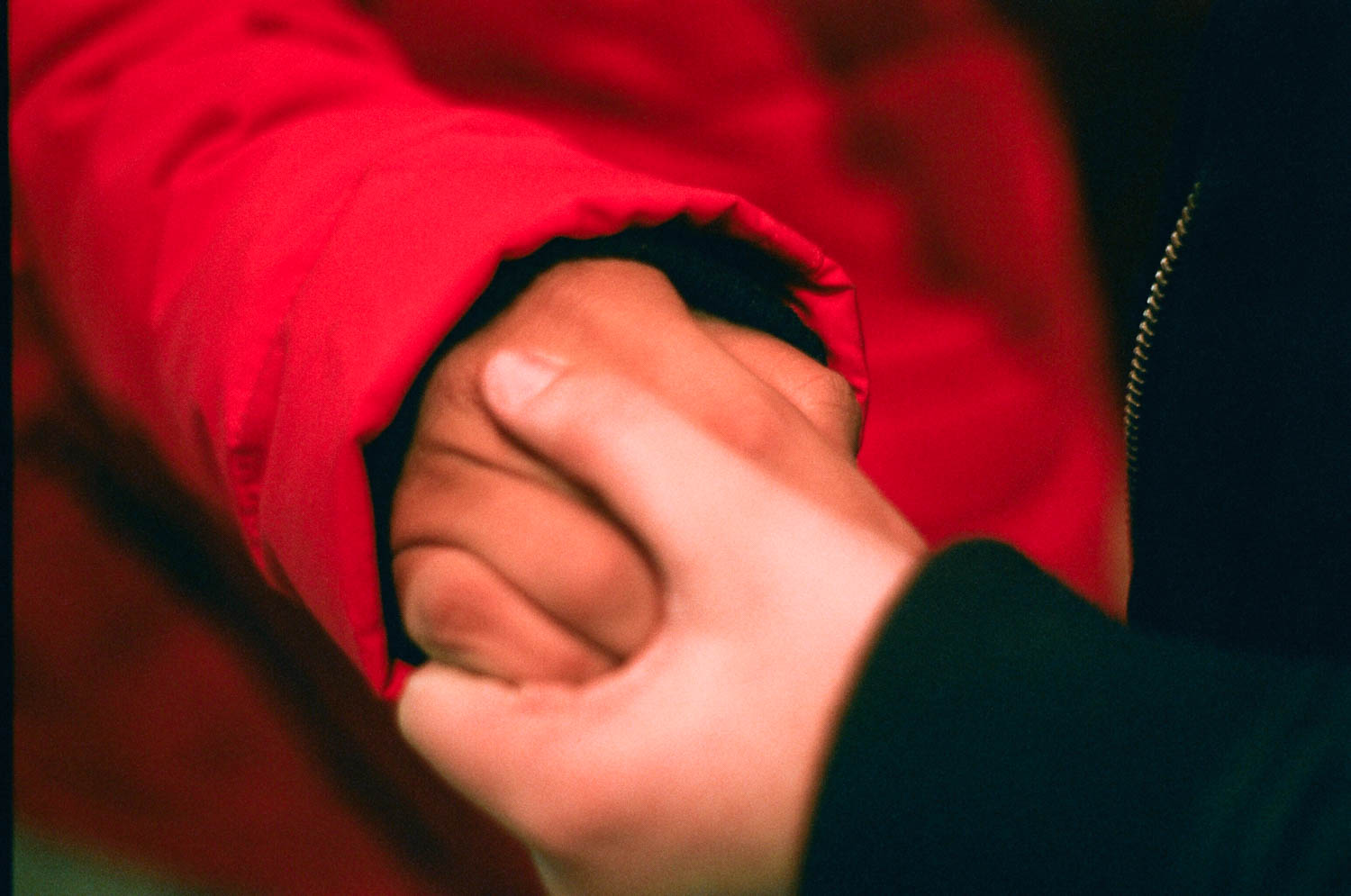 A close-up image of two people holding hands, one in a red jacket and the other in a black sweater.