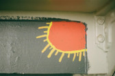 A painted orange sun outlined in yellow with light orange rays with a black background is visible in the upper corner of a ceiling with cyan moulding.