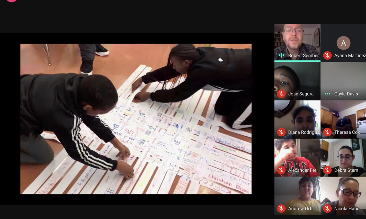 A screenshot of a video call presentation. Two students are placing strips of white paper together; they are creating a paper quilt. They are flanked on the right side by the images of ten individuals who are joining the call remotely.