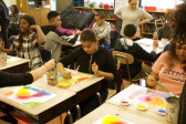 A classroom with several students, each at their own desk, painting with primary-color watercolors