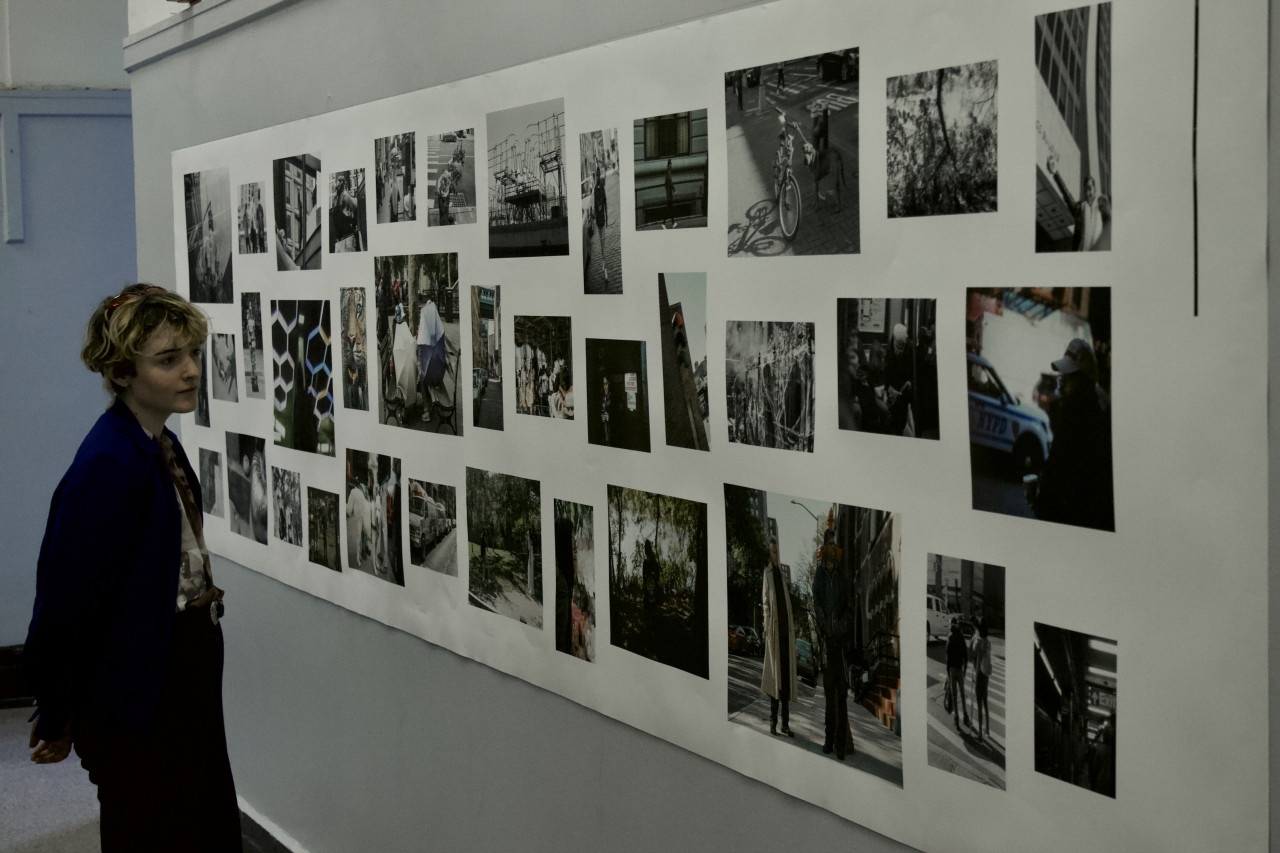 A person looks over an exhibition of photography arranged in a grid pattern on a wall