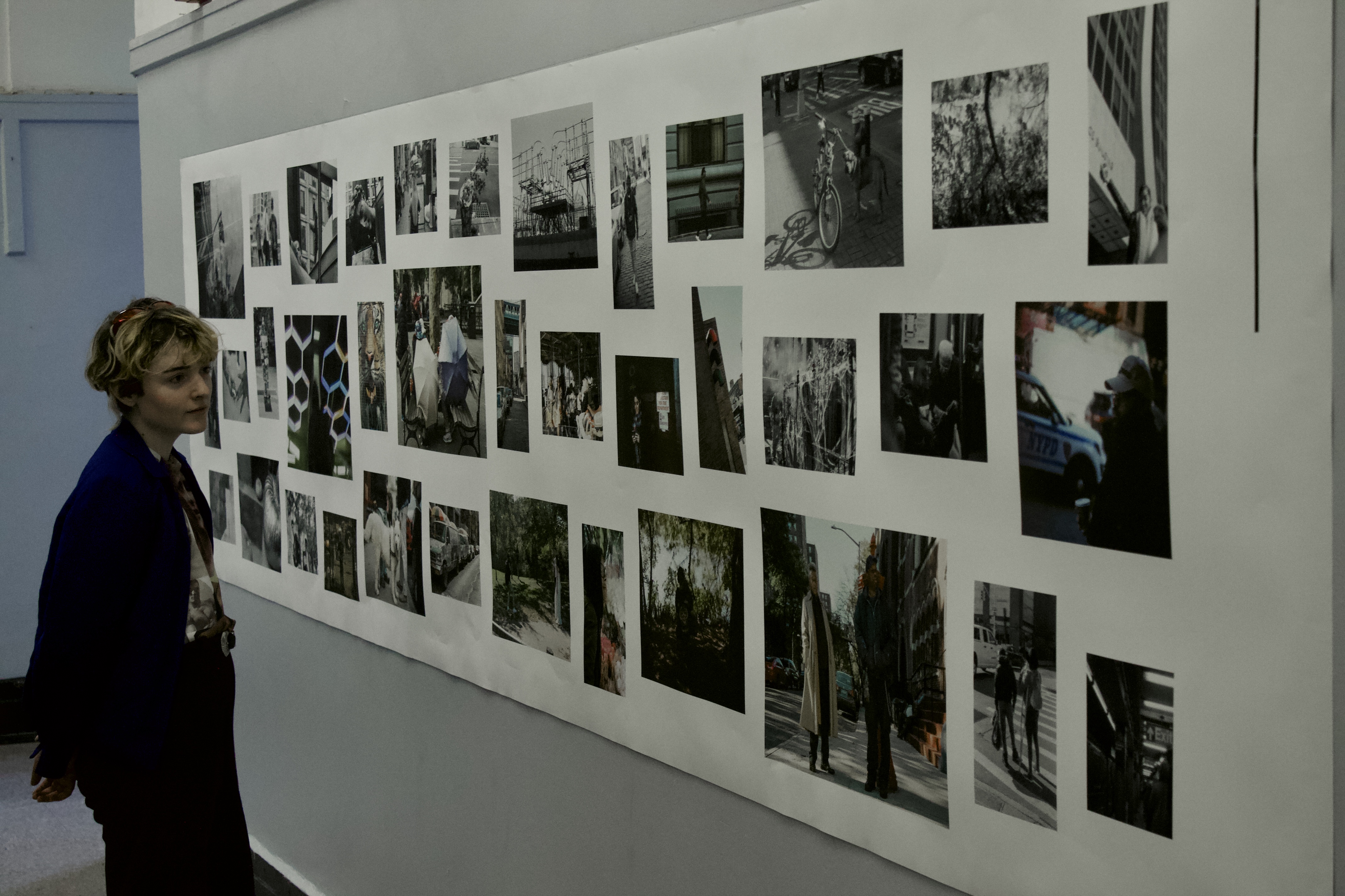 A person looks over an exhibition of photography arranged in a grid pattern on a wall