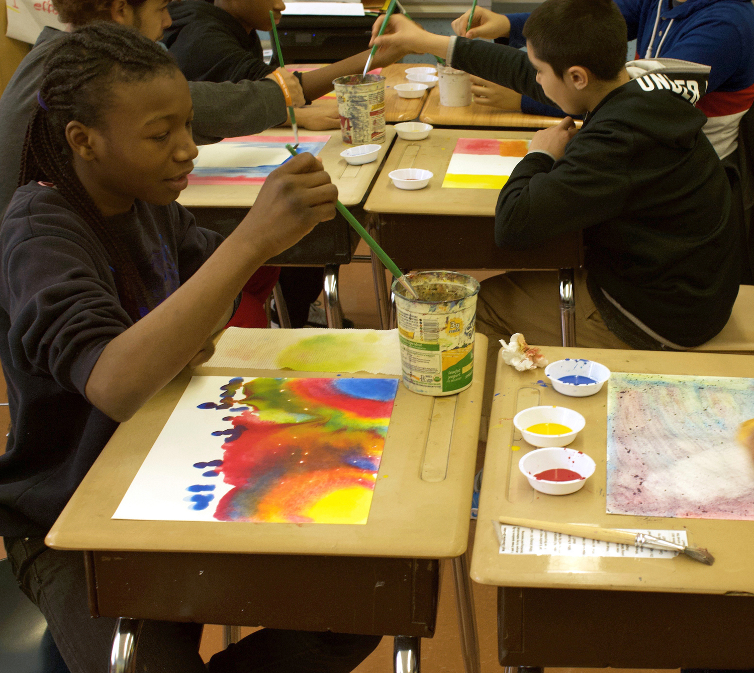 An image of several students paitning with watercolors, each on their own desk