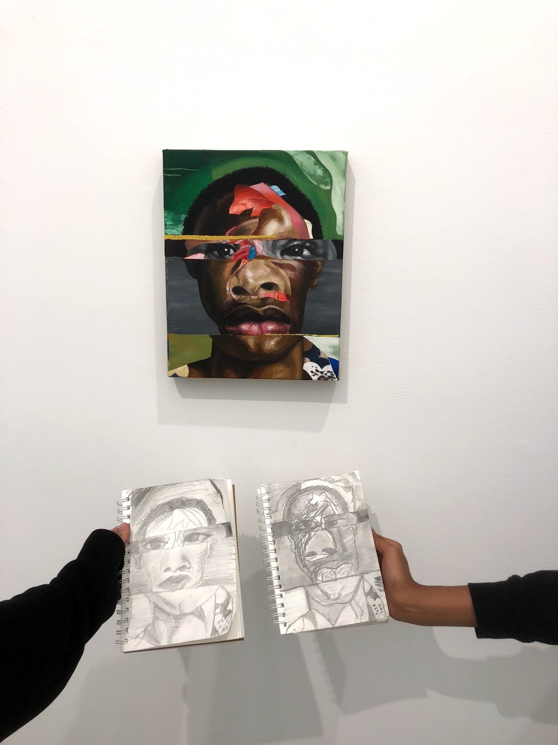 Two people hold up reproductions of a painting below the original that hangs on the wall. The painting depicts a collaged face obscured in parts by red, blue, and brown geometric shapes.