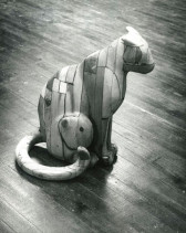 A black and white photograph of a wooden sculpture of a seated cat.