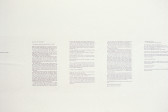Sheets of text hang on a white wall. Text is too small to be legible.