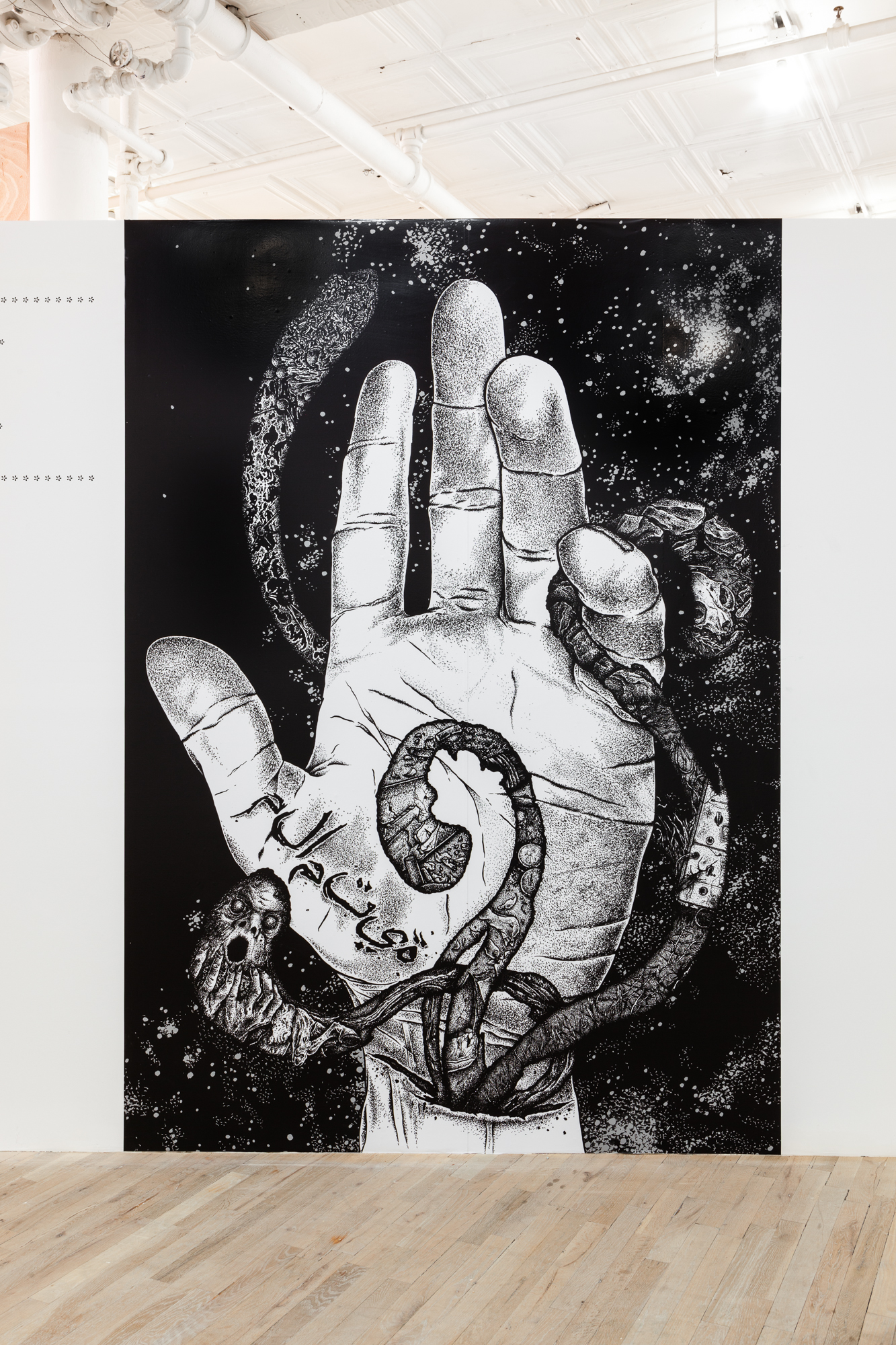 A large, black and white illustration of a hand displayed on a freestanding gallery wall. The hand extends upwards, palm facing the viewer, with tentacle like creatures escaping a slit on its wrist. The illustration extends across the full height of the wall.