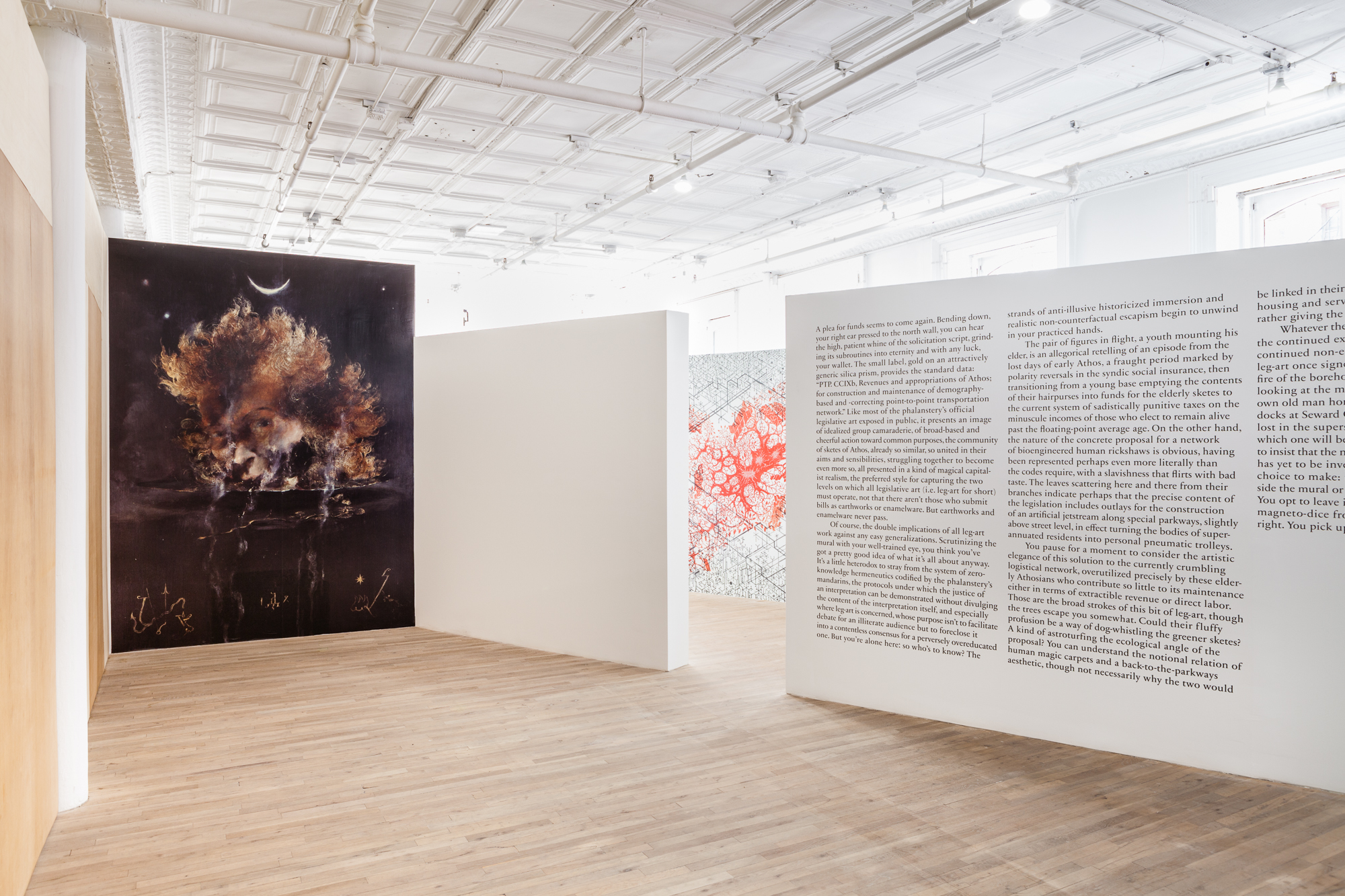 An angled view of a freestanding white wall displaying vinyl wall text in an exhibition space. The first sentence of the text reads, 