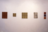 Five works depicting wood patterns in various tones are arranged in a horizontal line on a white wall.