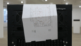 A moving gif of a paper diagram blowing from the wind of a computer device. The top right corner of the machine reads, 