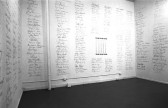Black and white image of a gallery enclave. The walls are covered with long lists of individual signatures that form several rows from floor to ceiling.