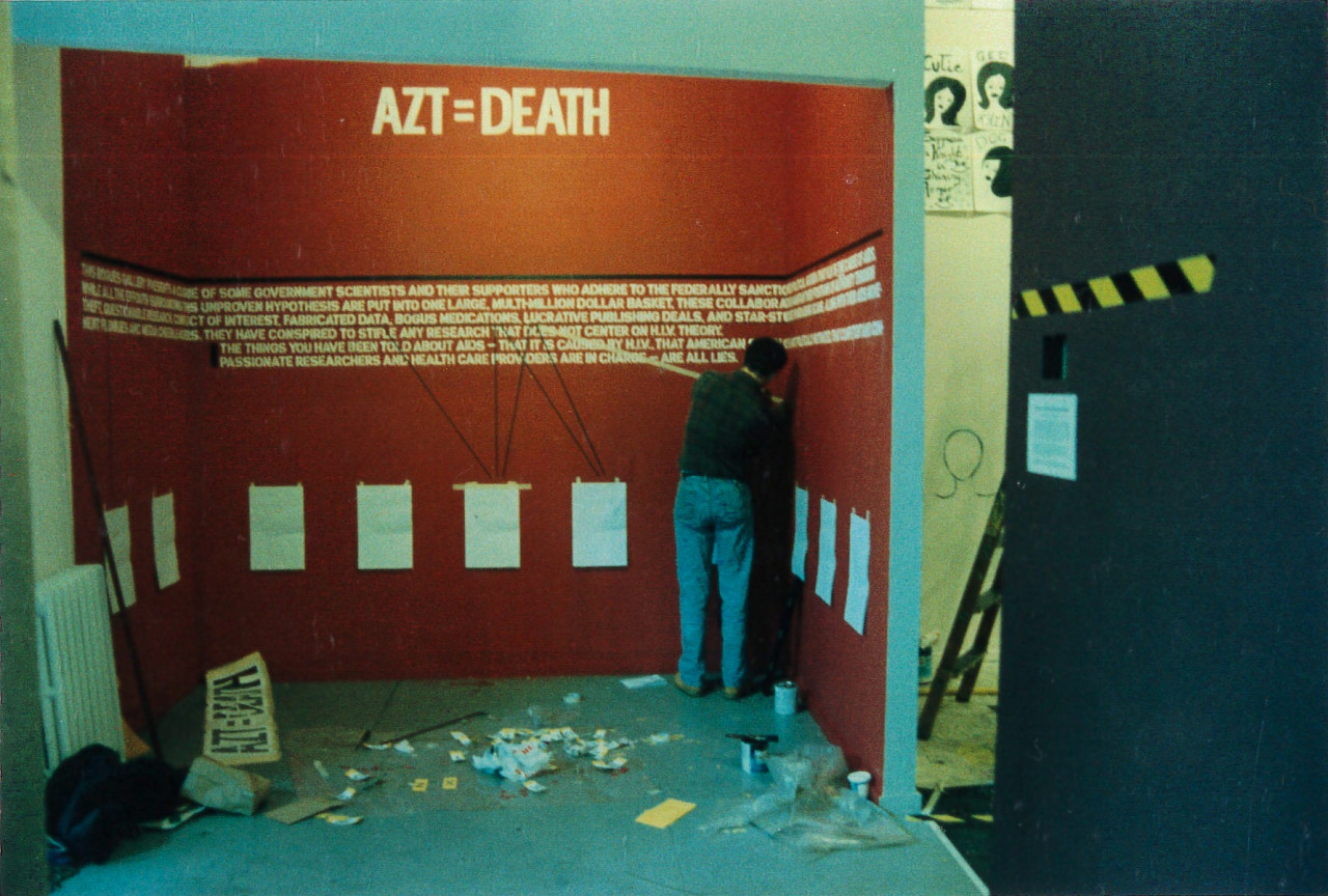 A person working in a small space enclosed by walls, painted red with white text. At the top of the wall, large letters read 