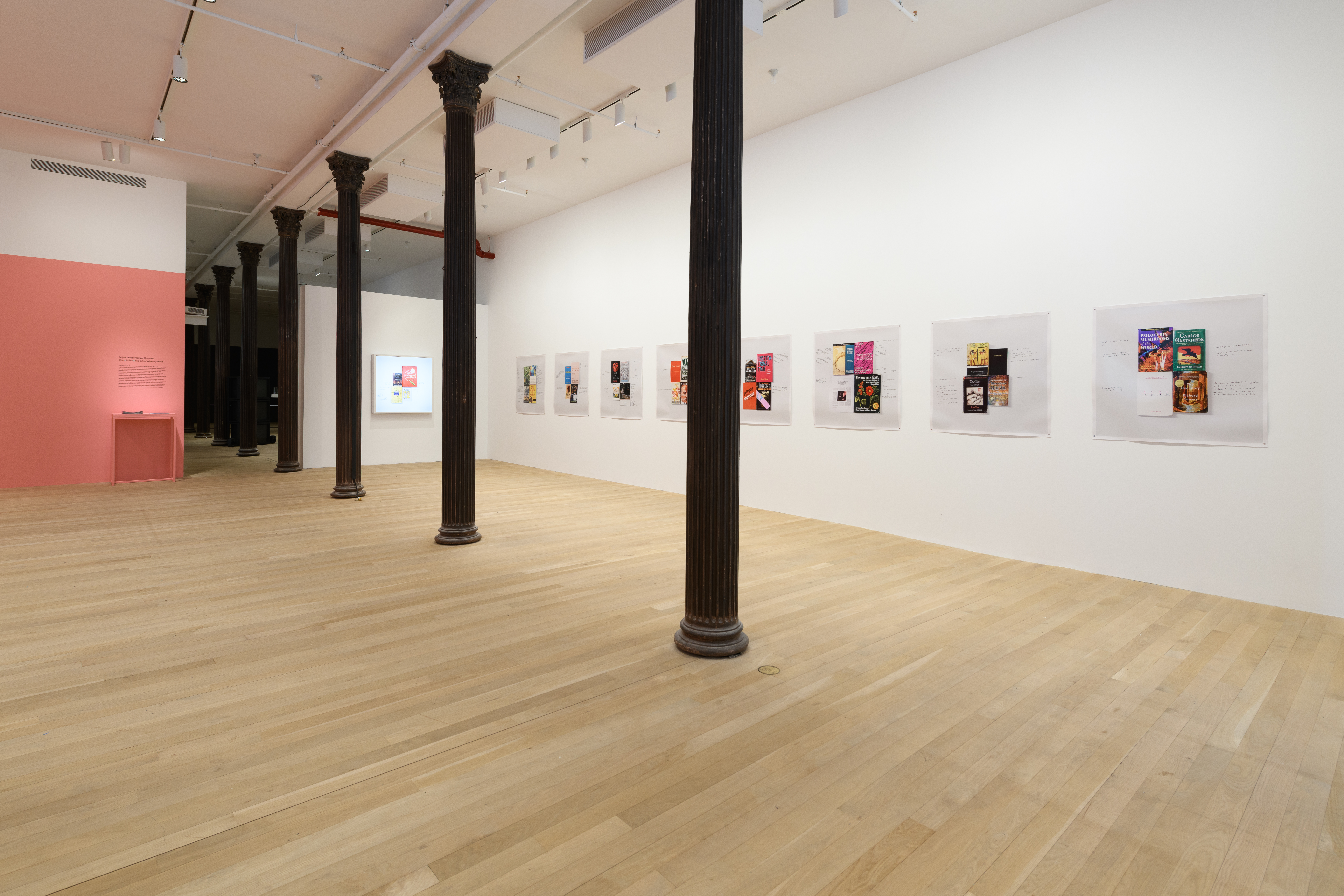 A photograph of a gallery space with eight prints hung on the rightmost wall and a lightbox mounted on the far wall.