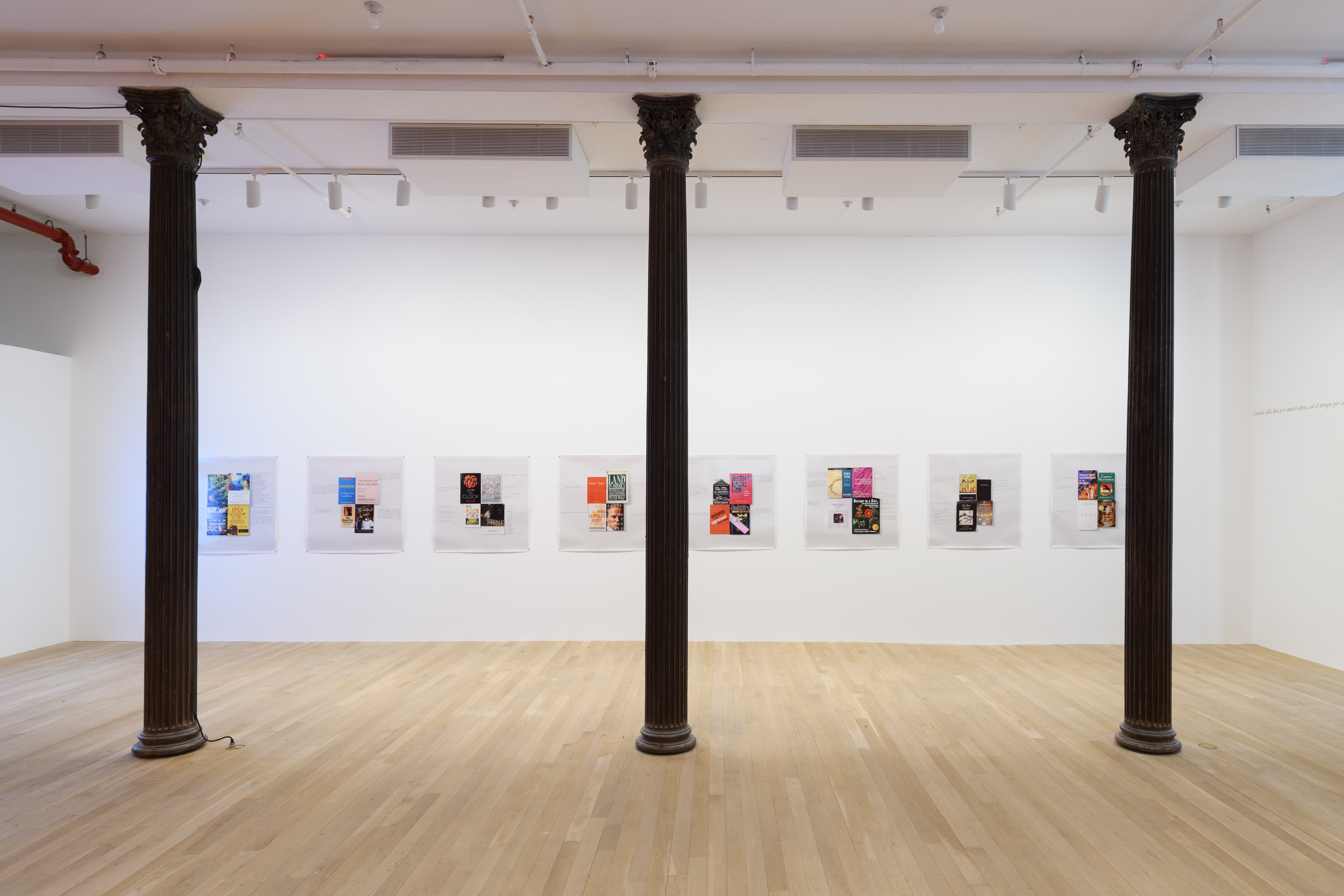 Eight digital prints are hung on a white gallery wall. In front of the wall are three floor-to-ceiling columns.