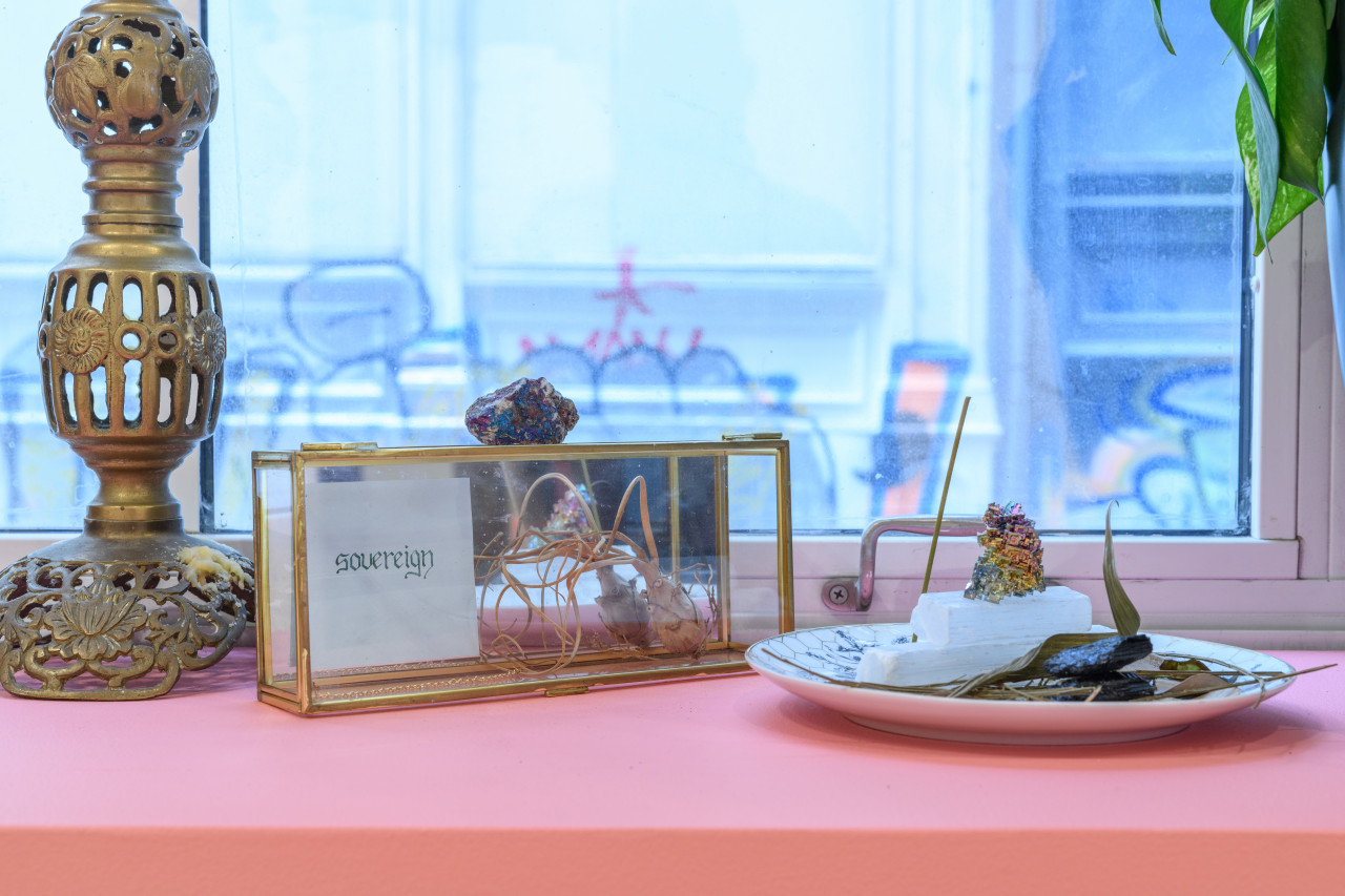 A candlestick holder, a small glass box and a plate with rocks and leaves sit on a windowsill.