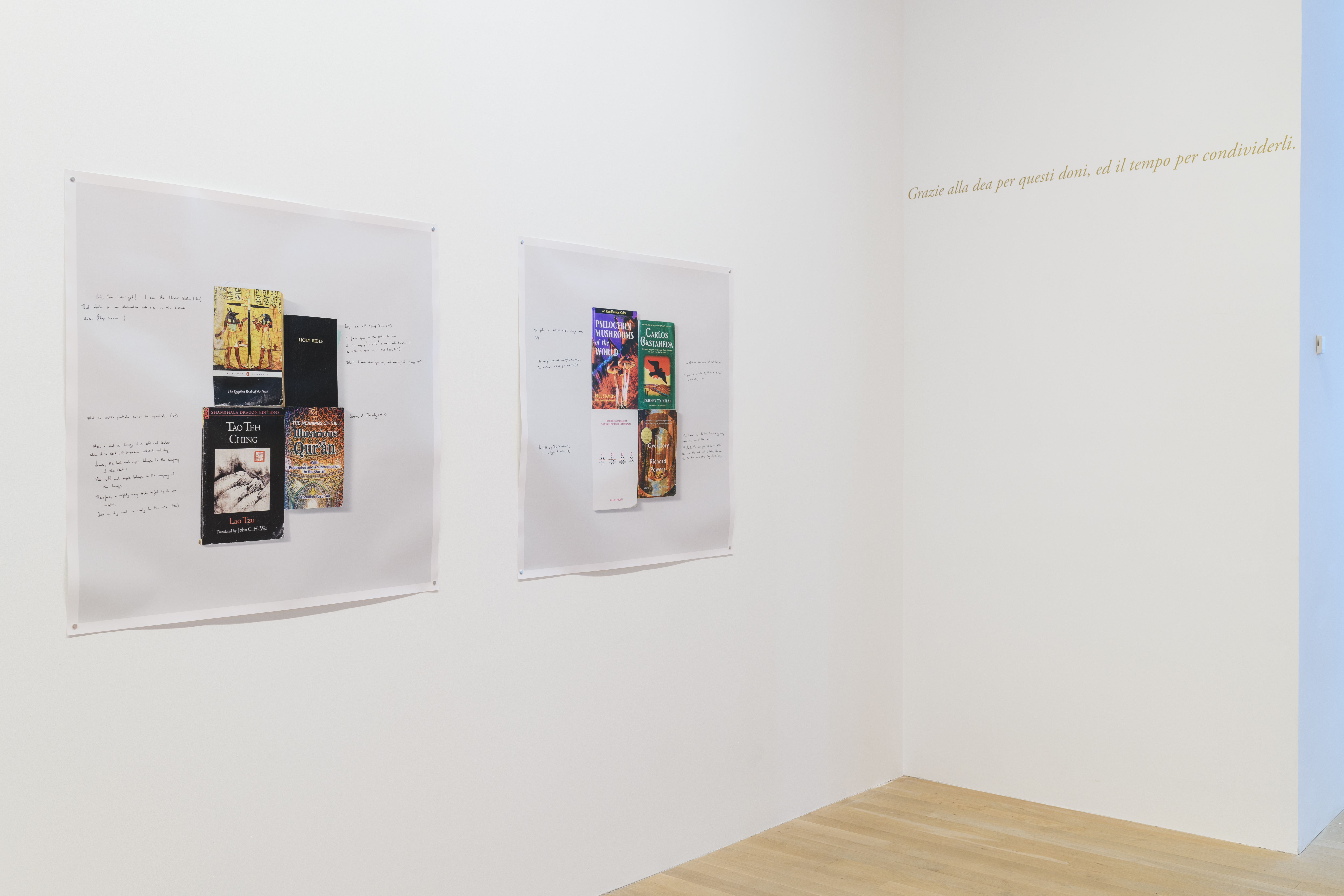 Two prints, of books with annotations written on the side, are hung on a white gallery wall.