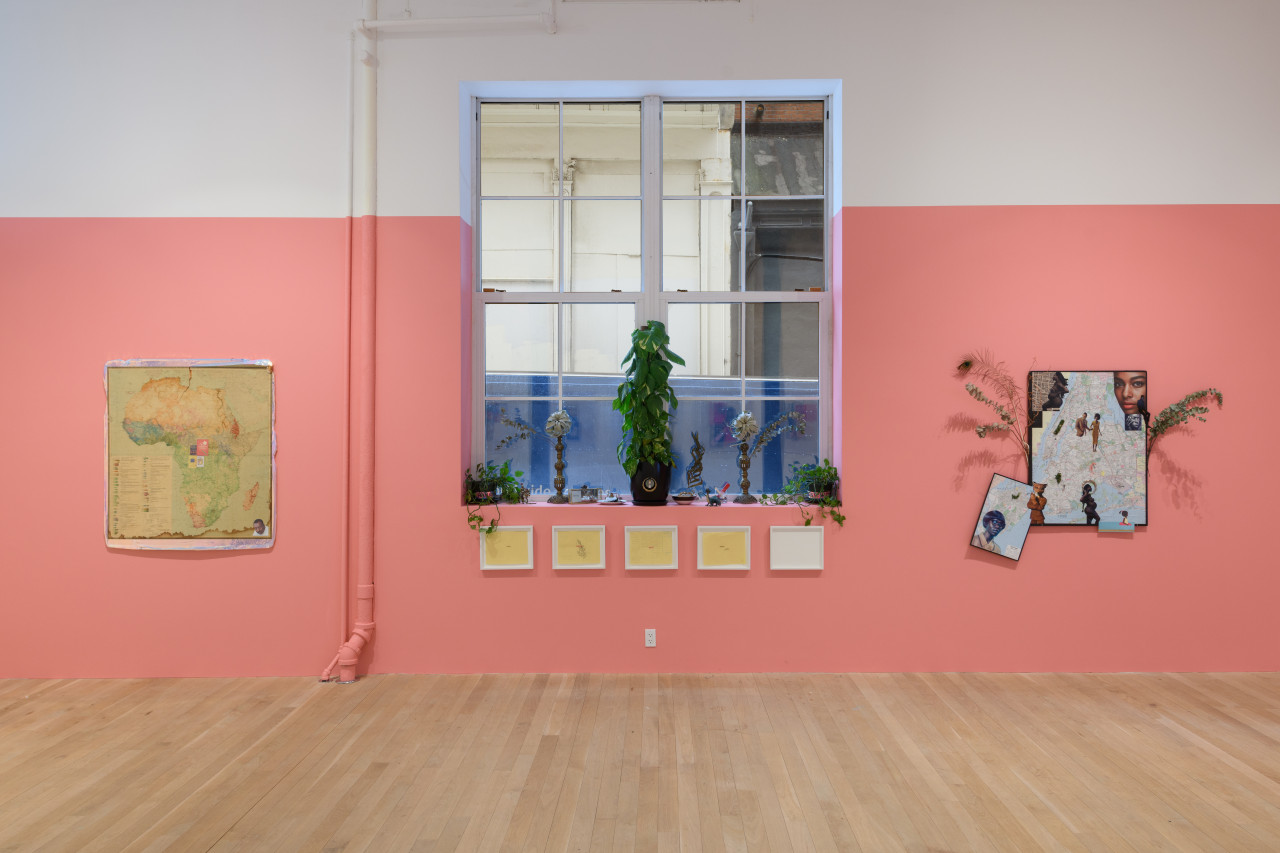 A gallery wall painted pink with a window in the middle. On the windowsill are several potted plants. Works on paper and a collage are hung on the wall.