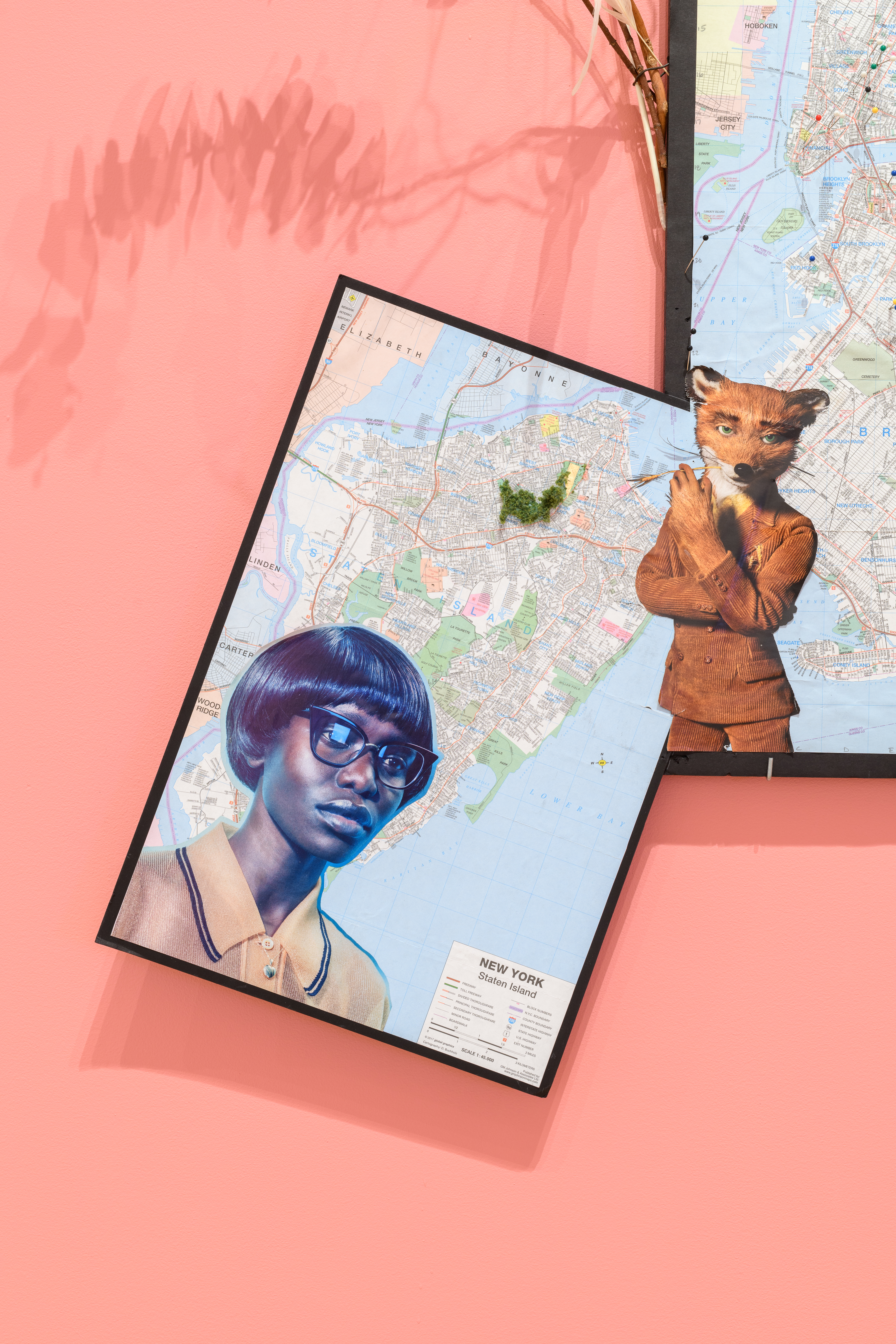A collage with a woman's figure in profile attached to a framed map, mounted on a pink gallery wall.