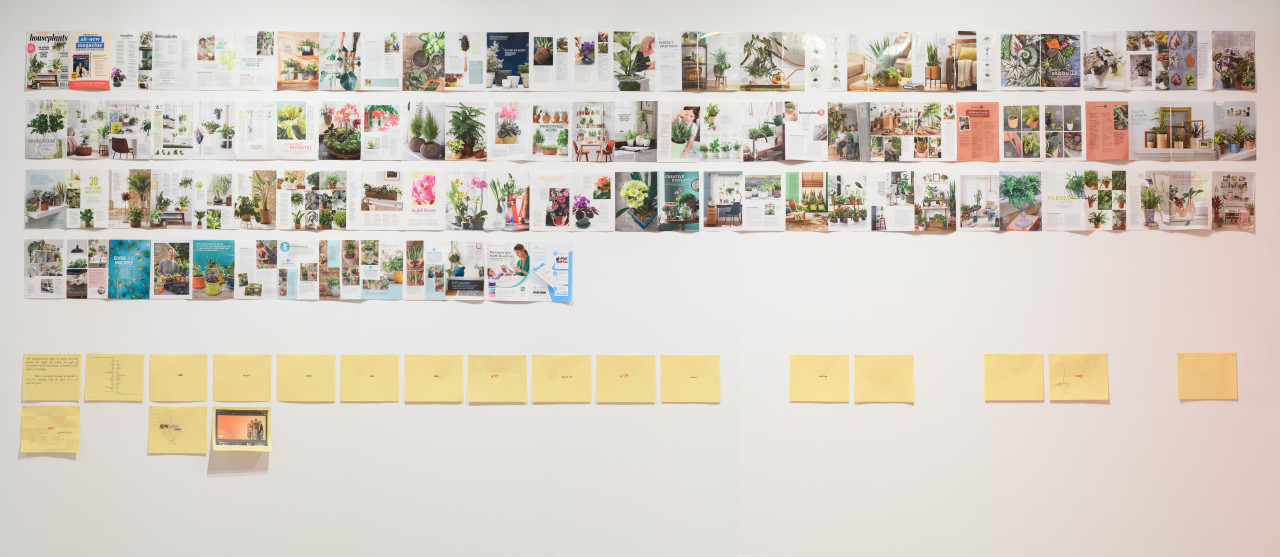 Magazine pages are arranged in several rows on a white gallery wall. Below the pages is a row of sketches on yellow paper.