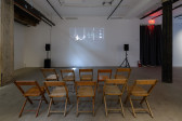 A set of wooden chairs arranged in the exhibition space to face projected film
