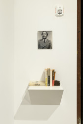 A picture of a man in a coat sits above a series of books on a shelf.