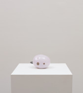A bulbous light-hued pink sphere-like object rests upon a white plinth. When in use, a red light on the object blinks to signal that the object is functioning correctly.