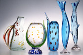 Five glass sculptures of varying colors arranged in a line. They are painted with small circular and oval dots.