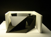 A model of a geometric, folded object with one mirrored side within an open white rectangle.