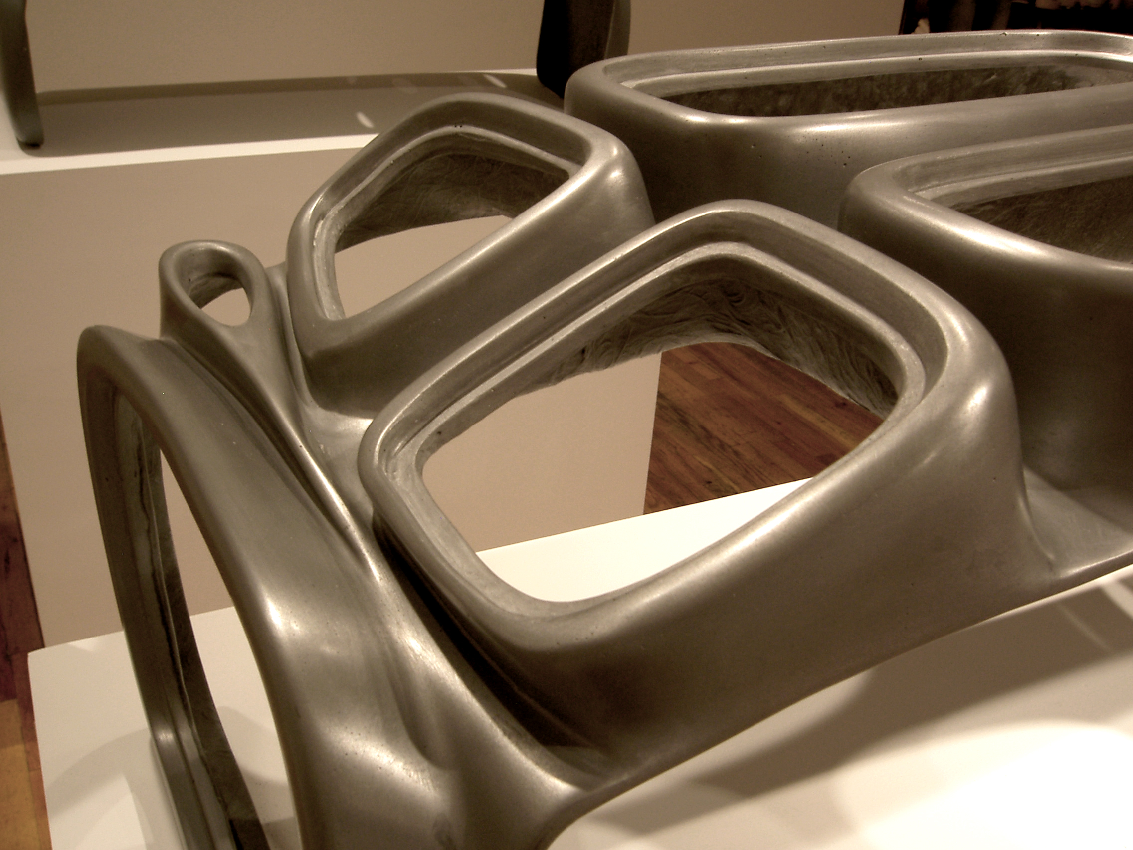 Detail view of a sculpture with a shiny grey finish. The shape of the sculpture forms a skeletal structure around amorphous square voids.