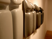 Detail view of four sculptures hung on the wall. The sculptures are ordered in neutral tones ranging from light to dark. Their shapes are approximately rectangular, each divided into quadrant segments.