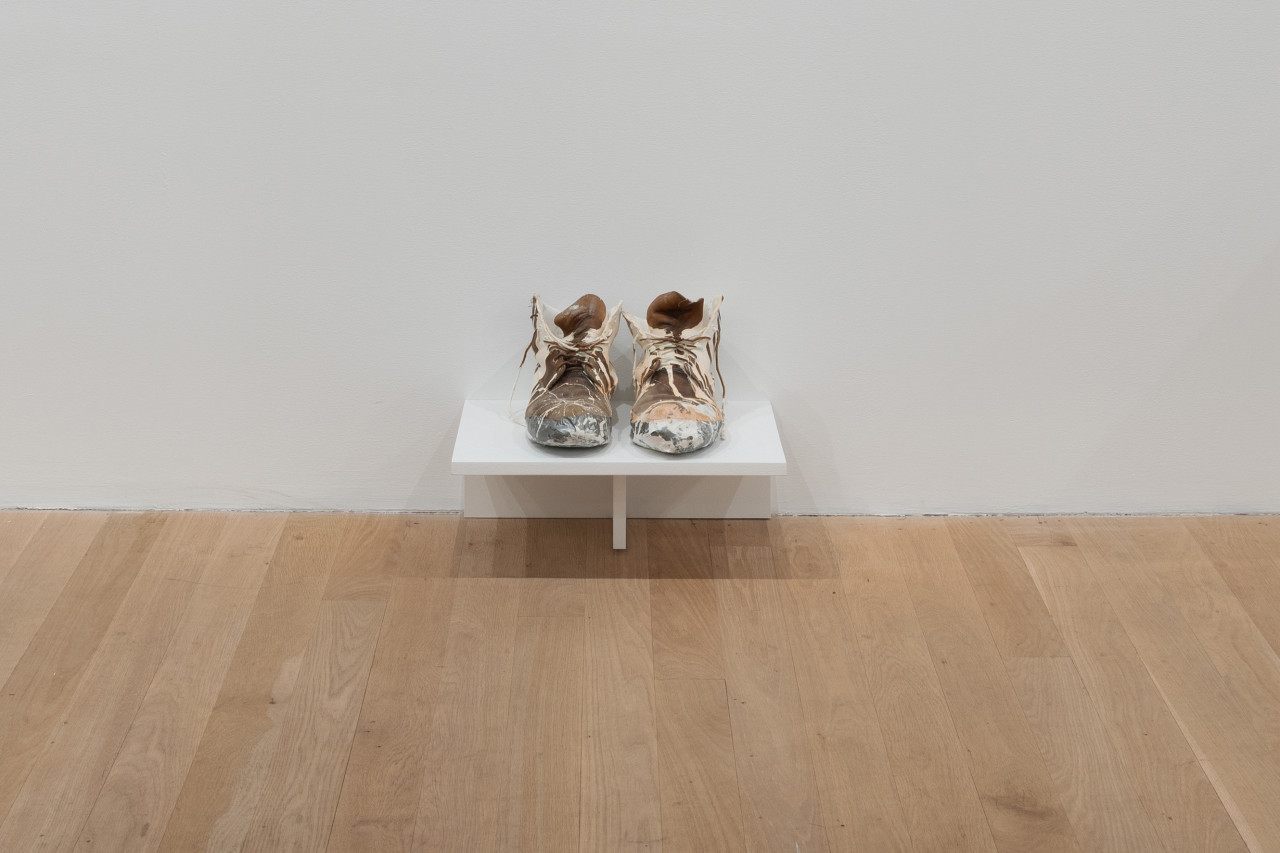 At the bottom of the gallery wall sits a small shelf housing a pair of construction boots that are extremely worn in and covered in white paint.