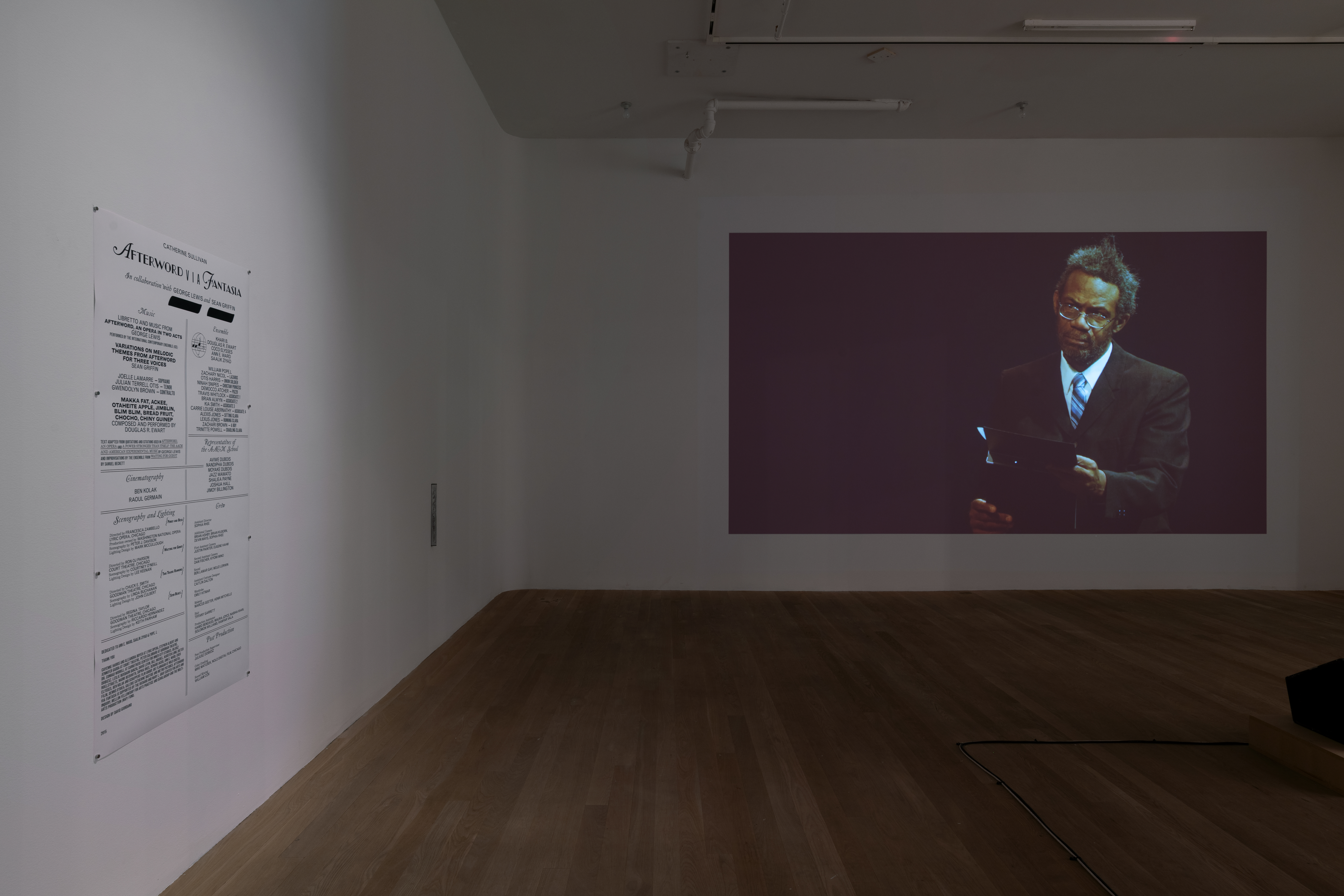 On the left gallery wall is a sheet of paper listing the credits of Catherine Sullivan's film 