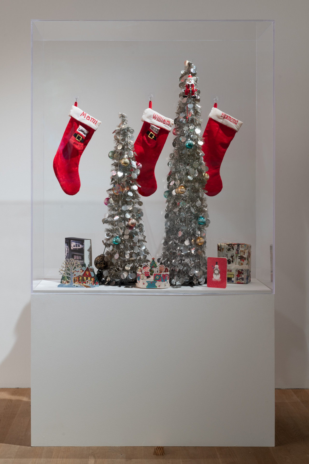 A display case holds three Christmas stockings labeled "Mami, William, and Desmond." There are two Christmas trees and cards at the bottom along with an assortment of Christmas paraphernalia.