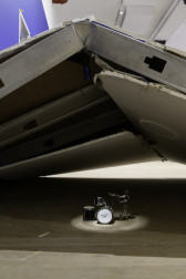 A small drum set lit by a spotlight sits underneath a demolished wall.
