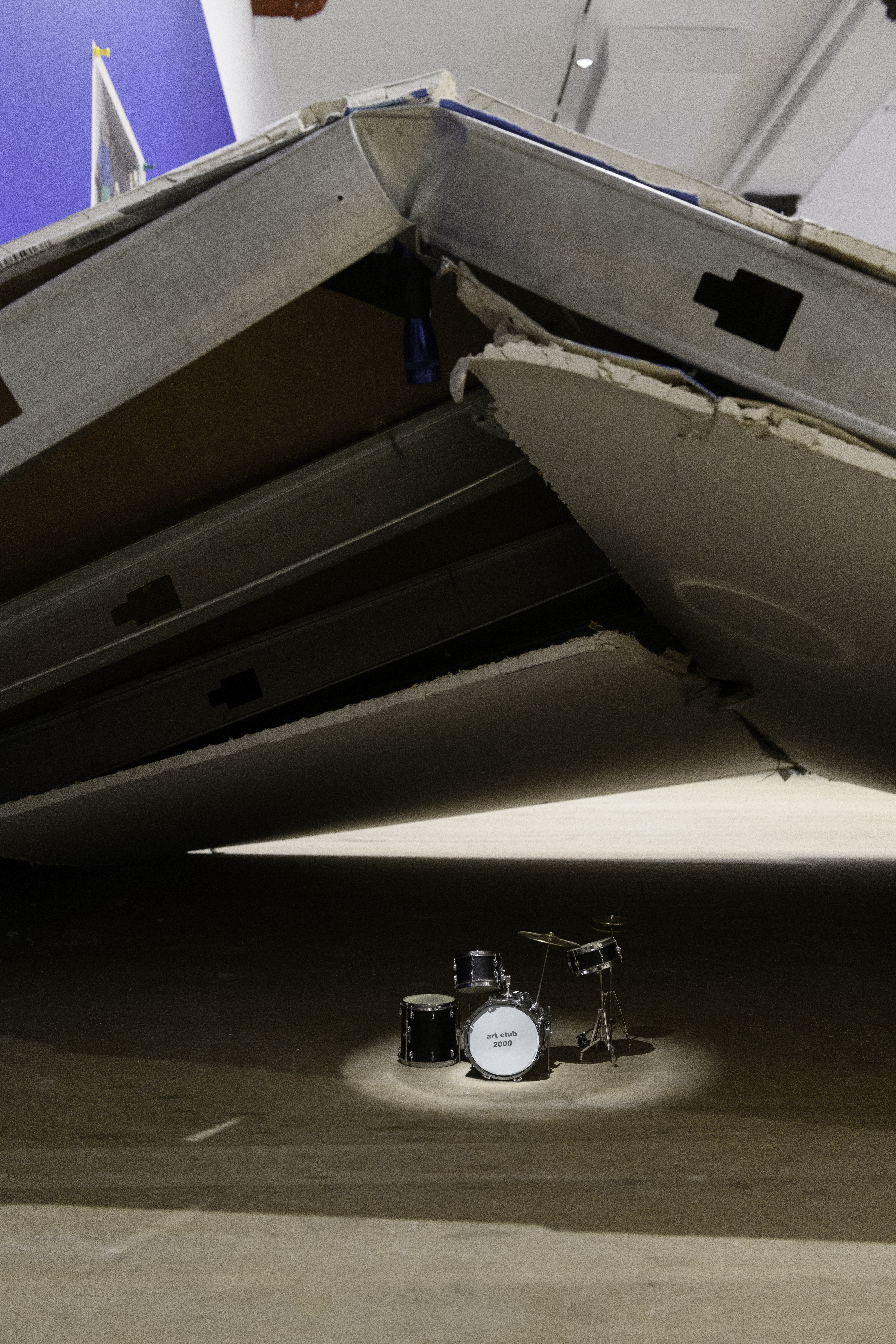 A small drum set lit by a spotlight sits underneath a demolished wall.