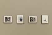 A display of four black and white photographs on a beige gallery wall.