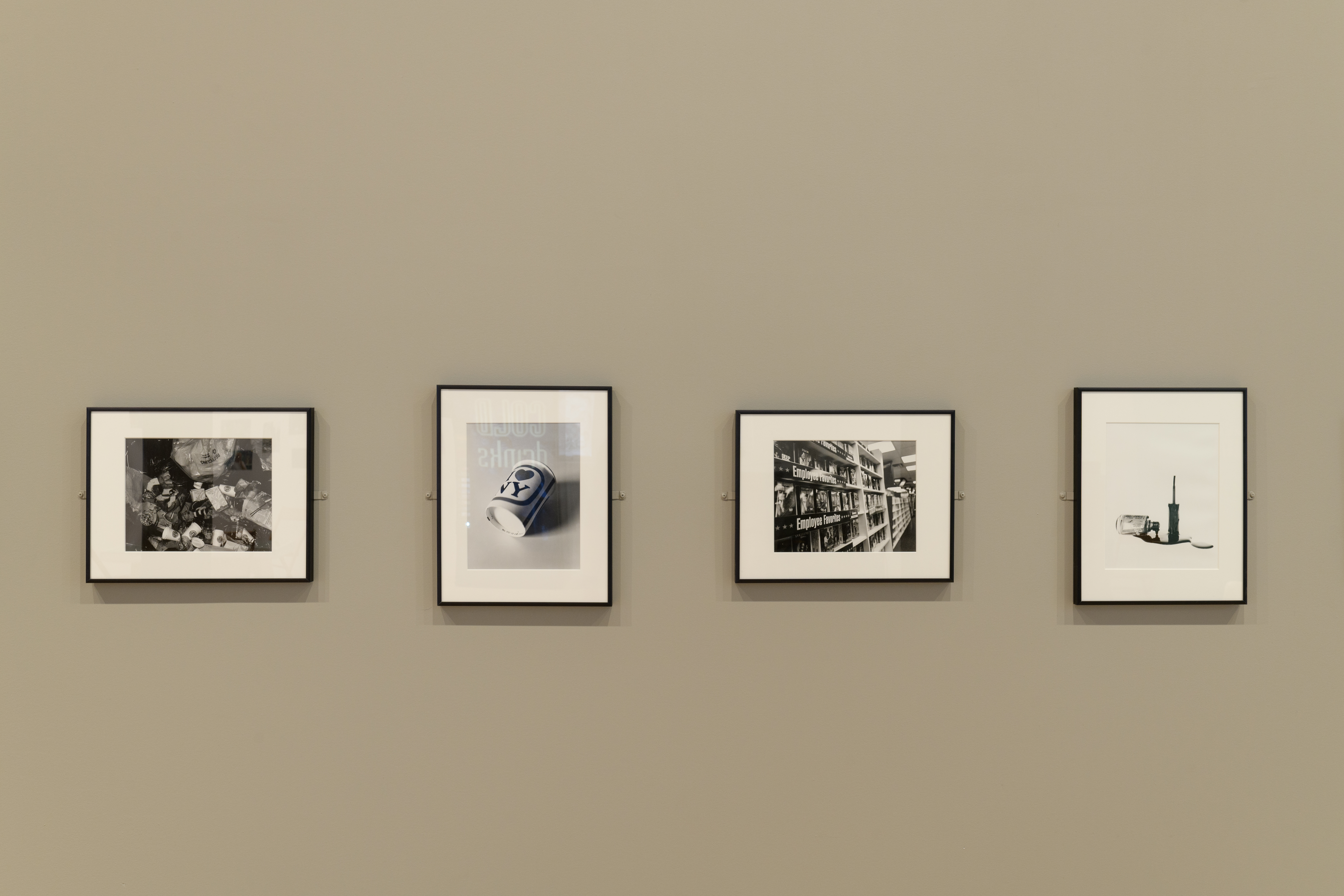 A display of four black and white photographs on a beige gallery wall.