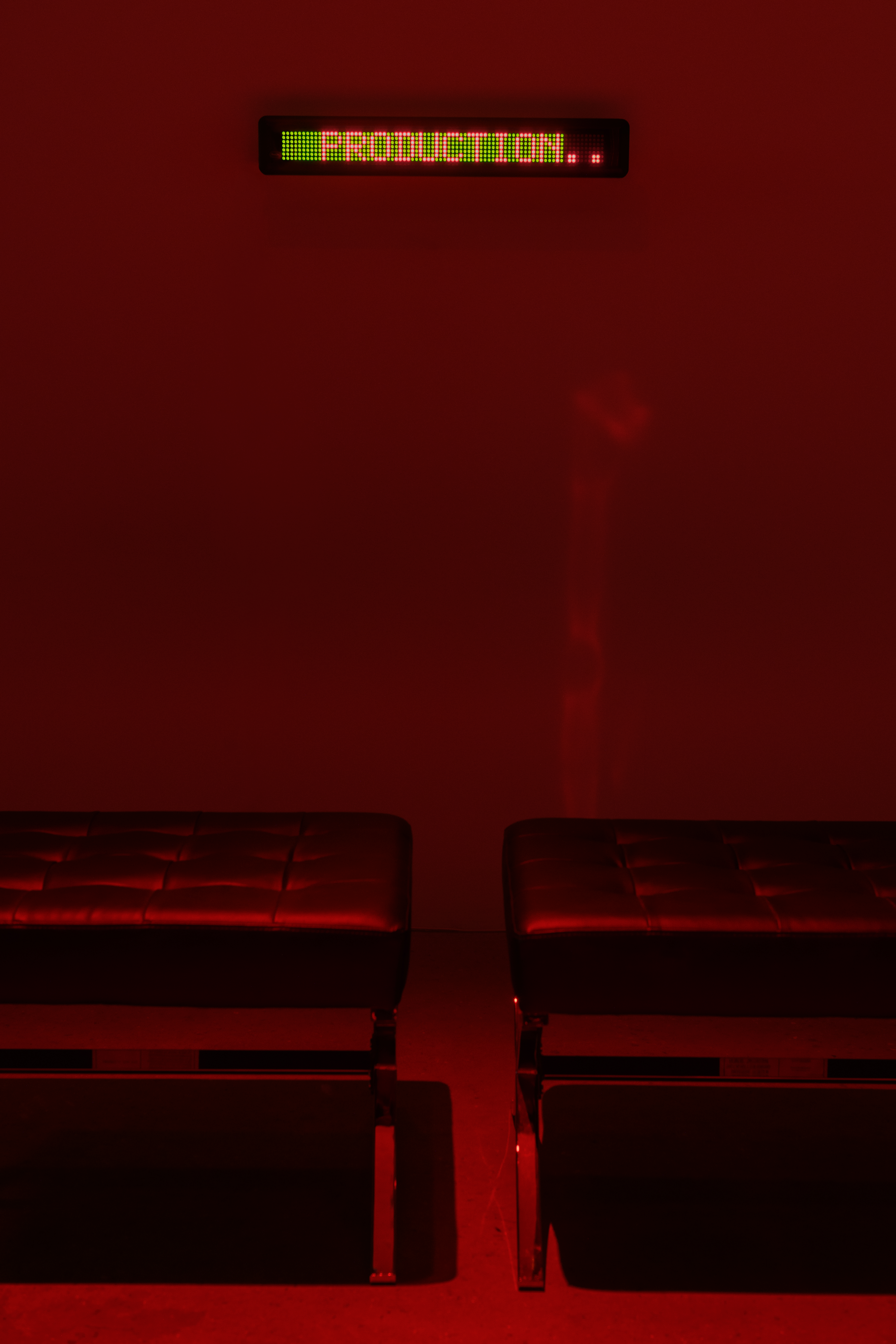 A view of two black leather stools in front of an LED sign crawl of a text.