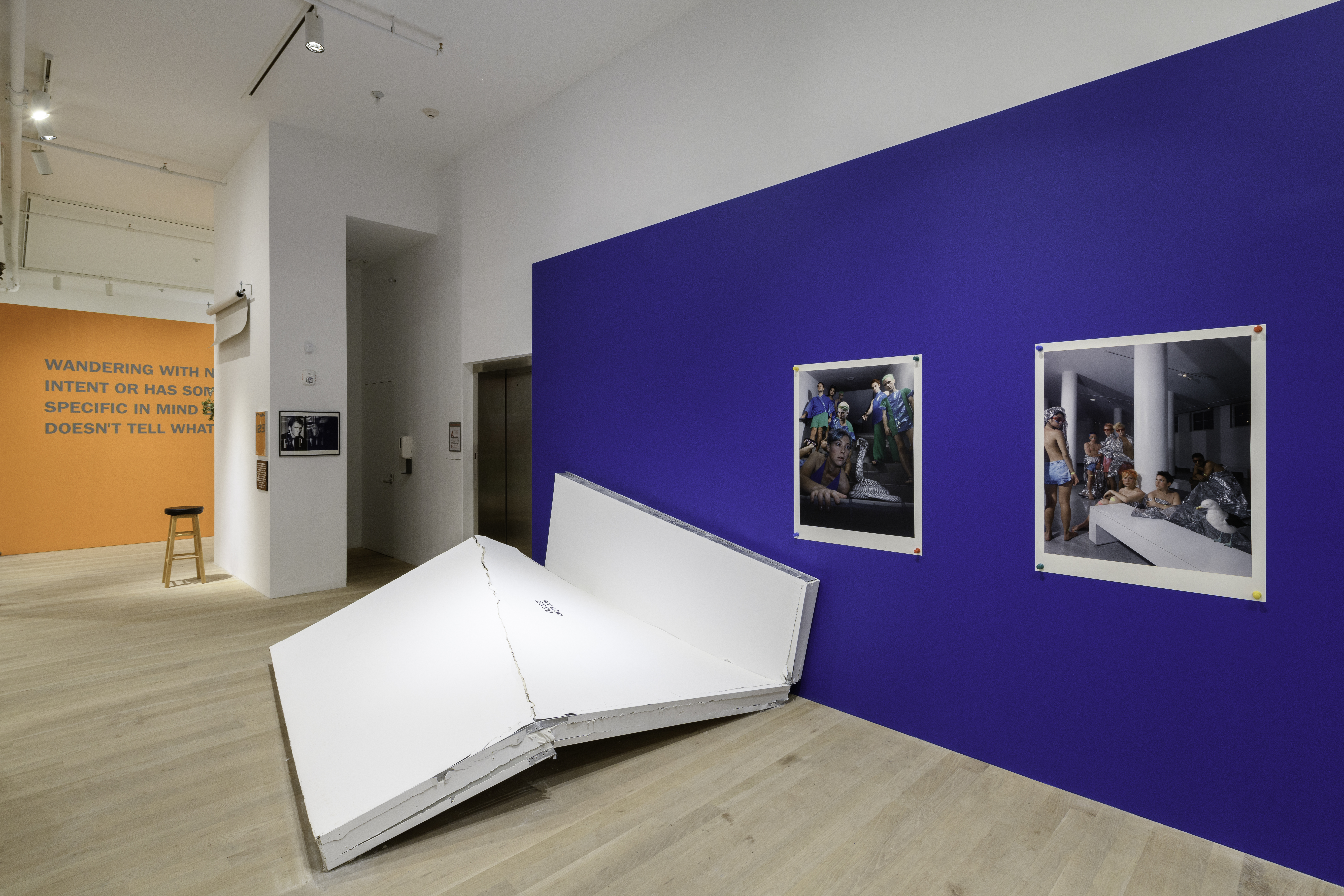 A view of multiple works including a blue gallery wall displaying dynamic images hung by large push pins and a demolished wall.