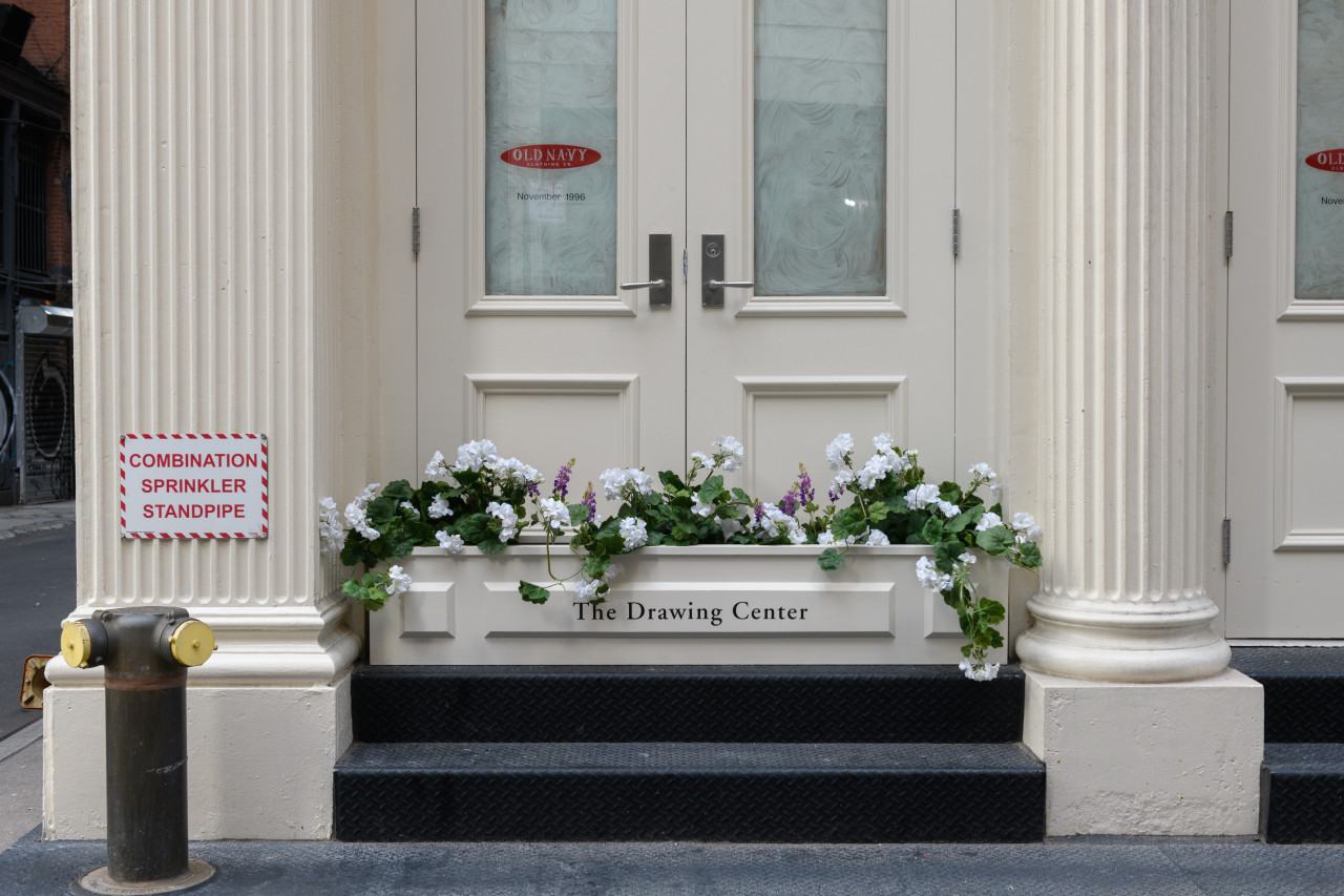 An off white planter reading "The Drawing Center" sits beneath a glazed over window displaying the Old Navy logo.