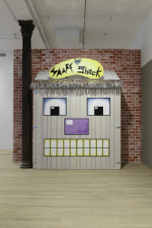 A view of a built shack structure displaying a colorful cartoon face and a graphic sign that reads 