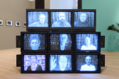 A display of nine CRT monitors showing nine individuals in a bluish hue.