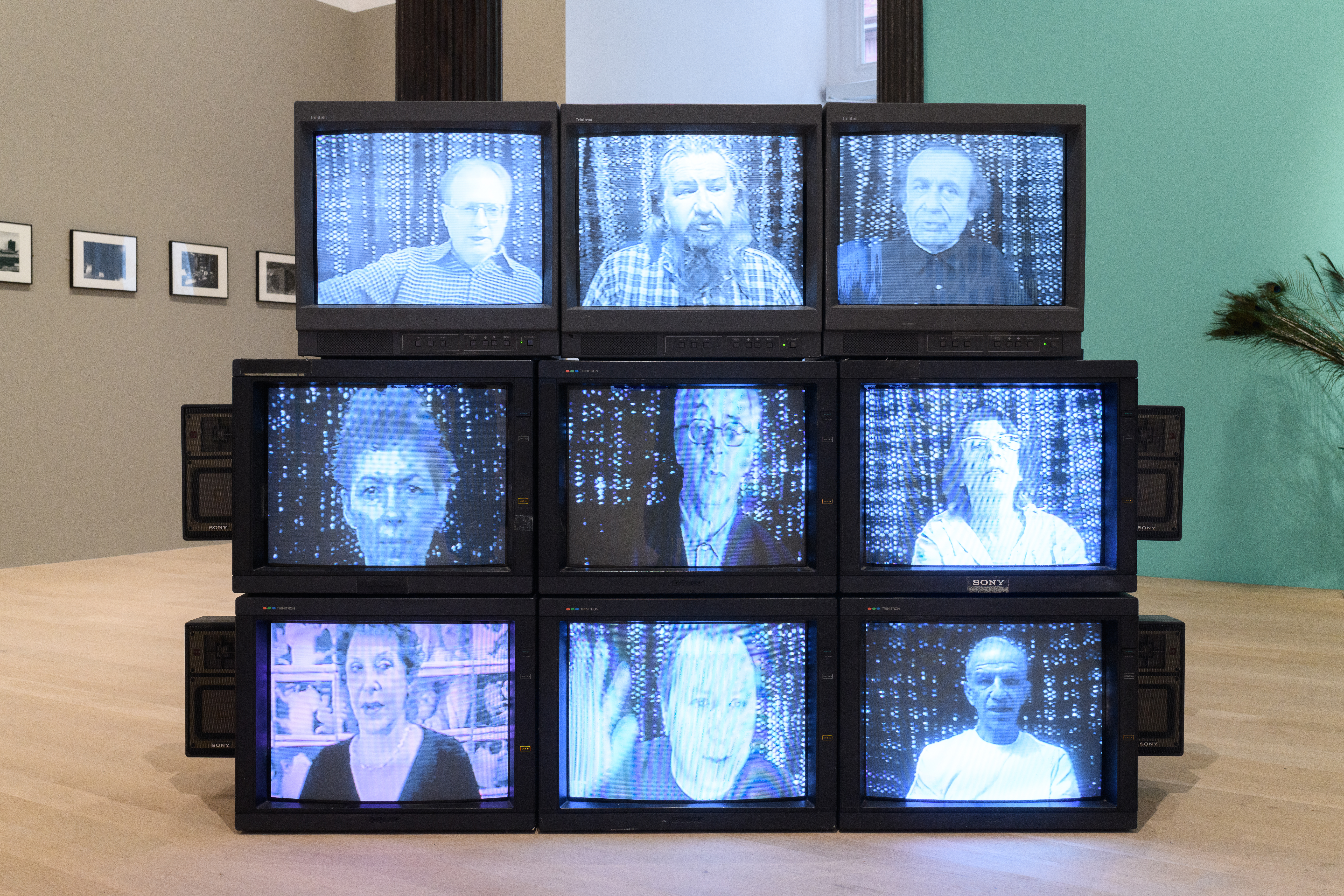 A display of nine CRT monitors showing nine individuals in a bluish hue.