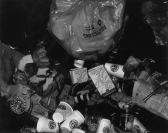 A pile of trash, including Starbucks cups, empty packs of cigarettes, newspaper, and food remnants, is strewn across the ground.