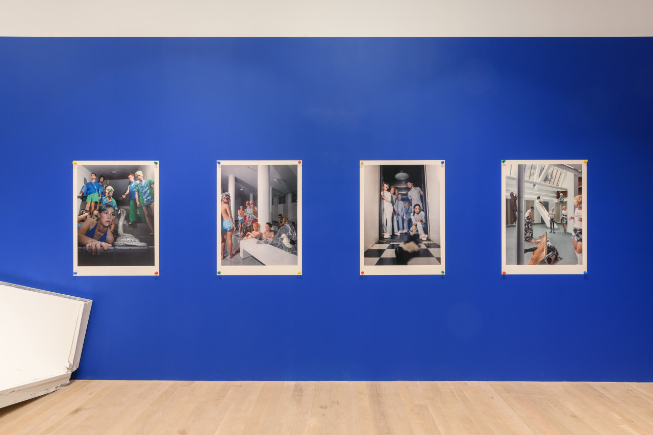 Four dynamic images of a group of individuals pinned by large push pins on a blue gallery wall.