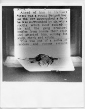 A photograph of a short printed text. In front of the text is a doll lying in supine position.