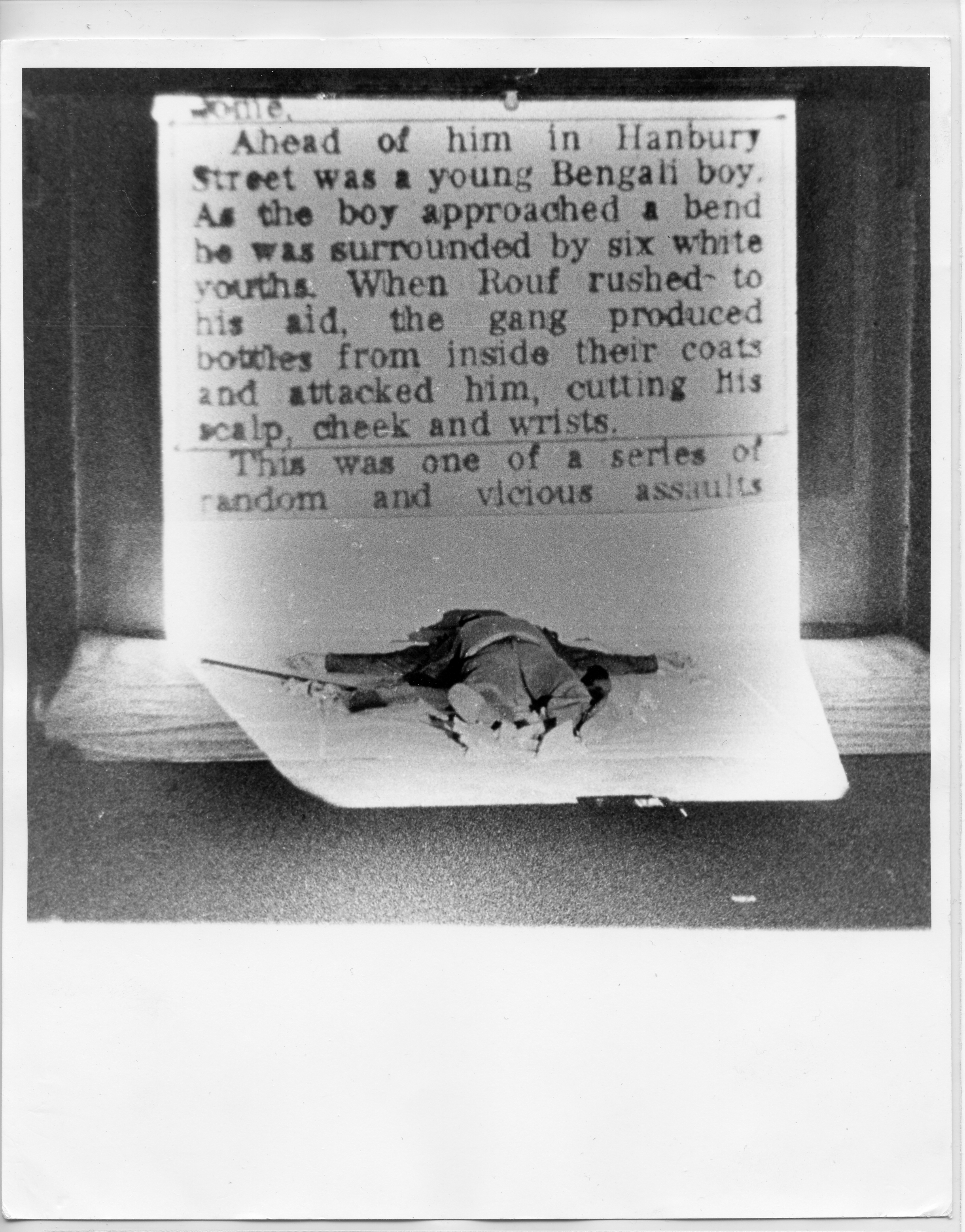 A photograph of a short printed text. In front of the text is a doll lying in supine position.